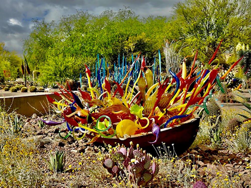 An outdoor sculpture display made from intricate pieces of glass surrounded by greenery.