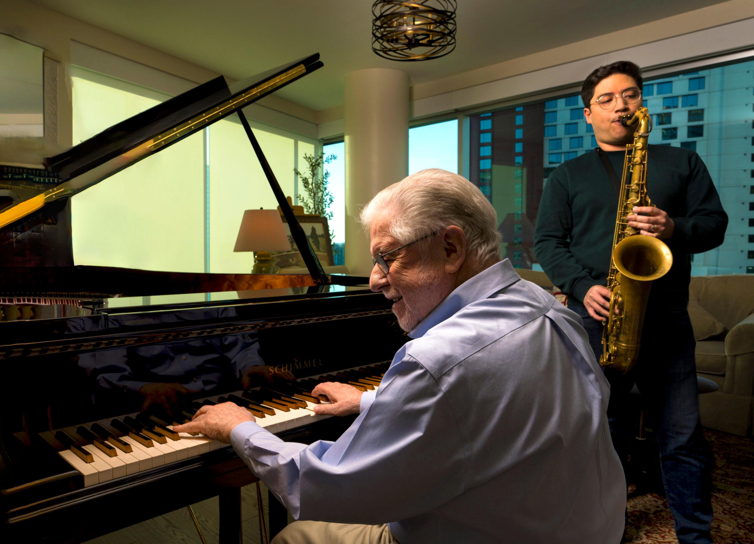 A man plays a grand piano while another man plays the saxophone.