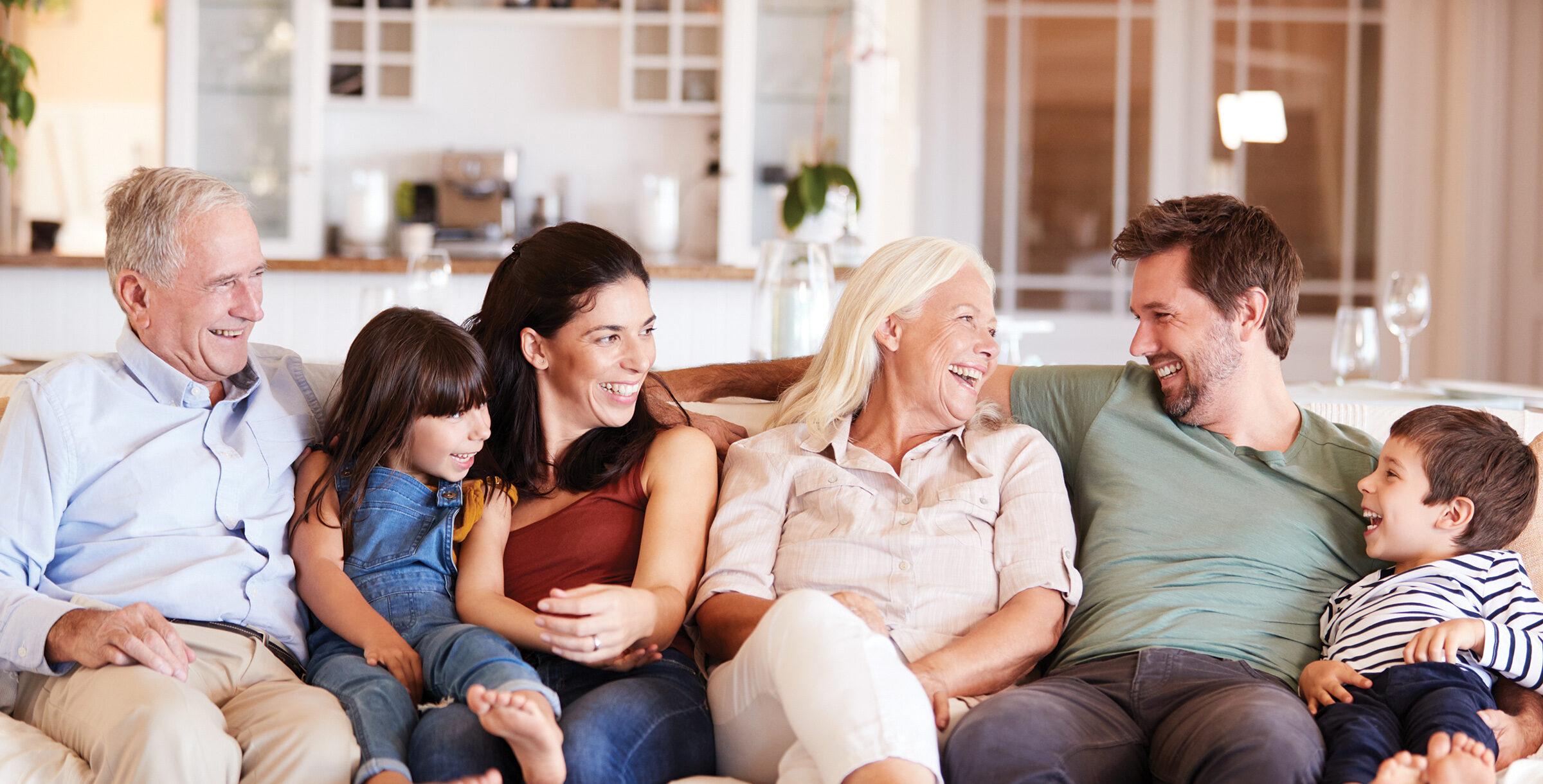 A happy three-generation family sits on a sofa and looks at each other, front view.