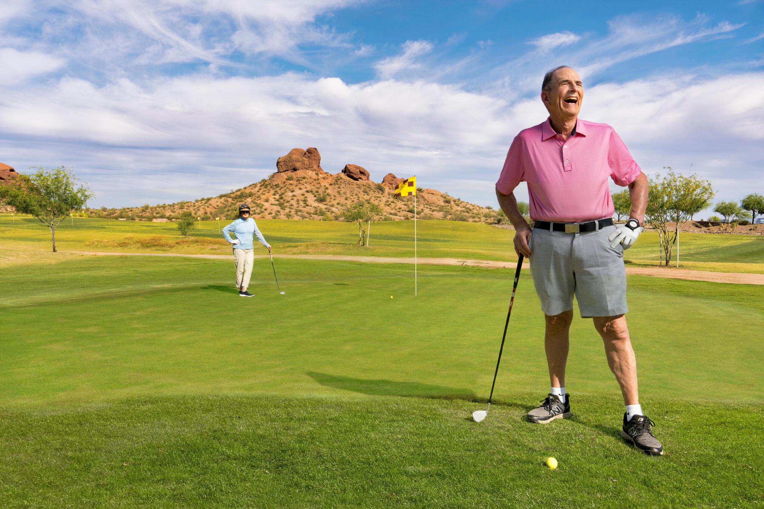 Two happy older adults stand on a golf course.