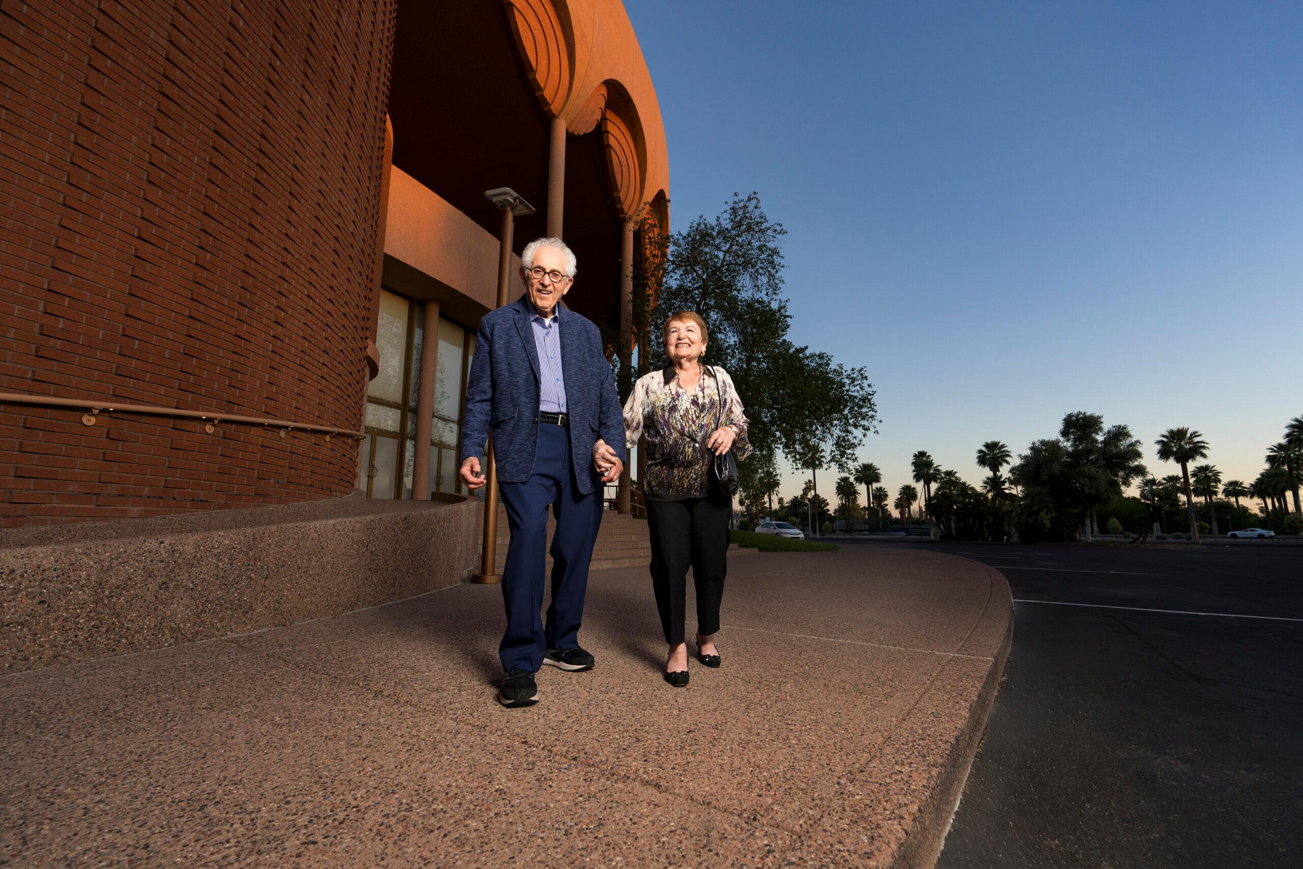 A smiling couple walks out of the theater at dusk.