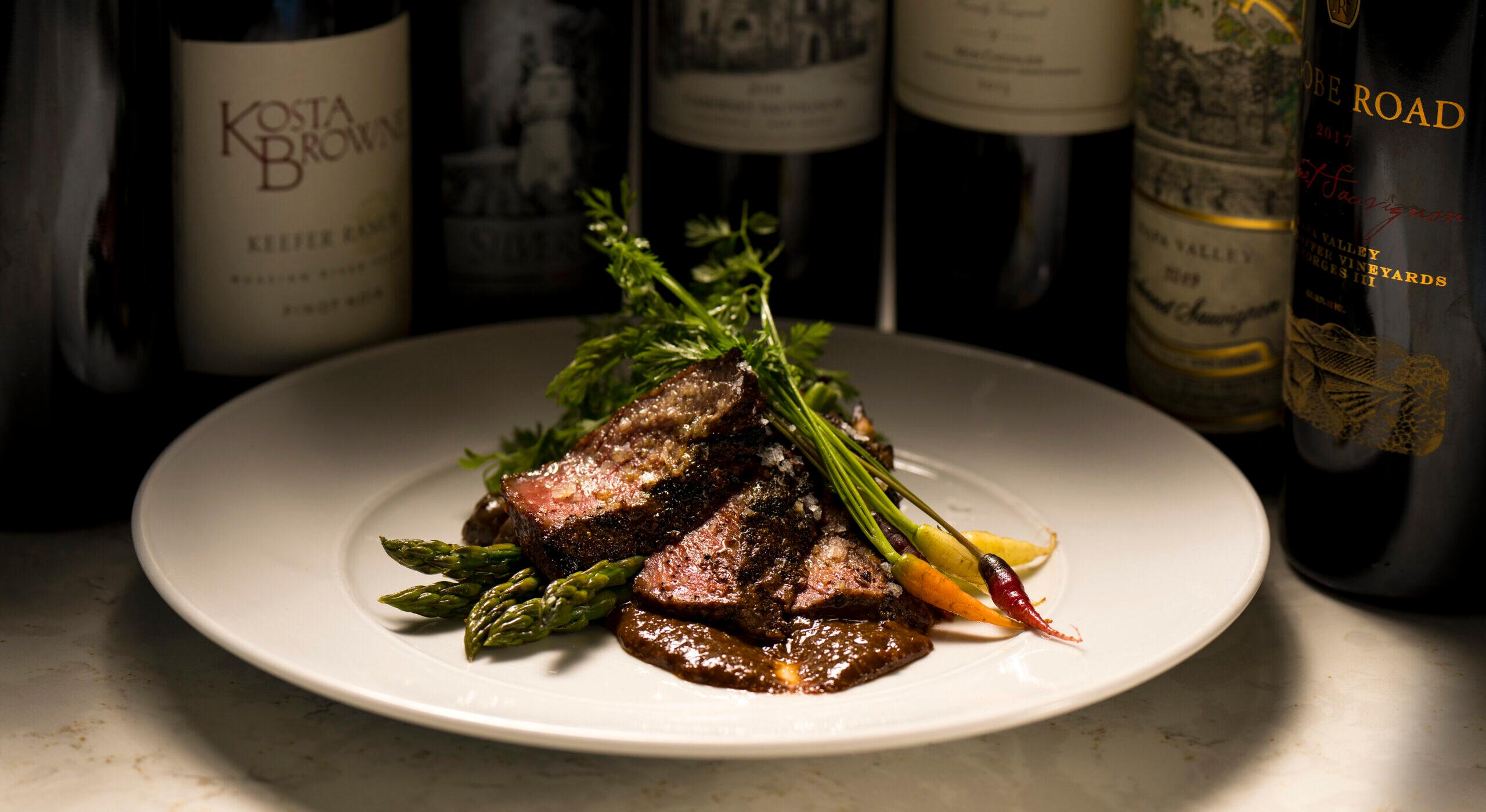 A gourmet steak dish surrounded by fancy wine bottles in the background.