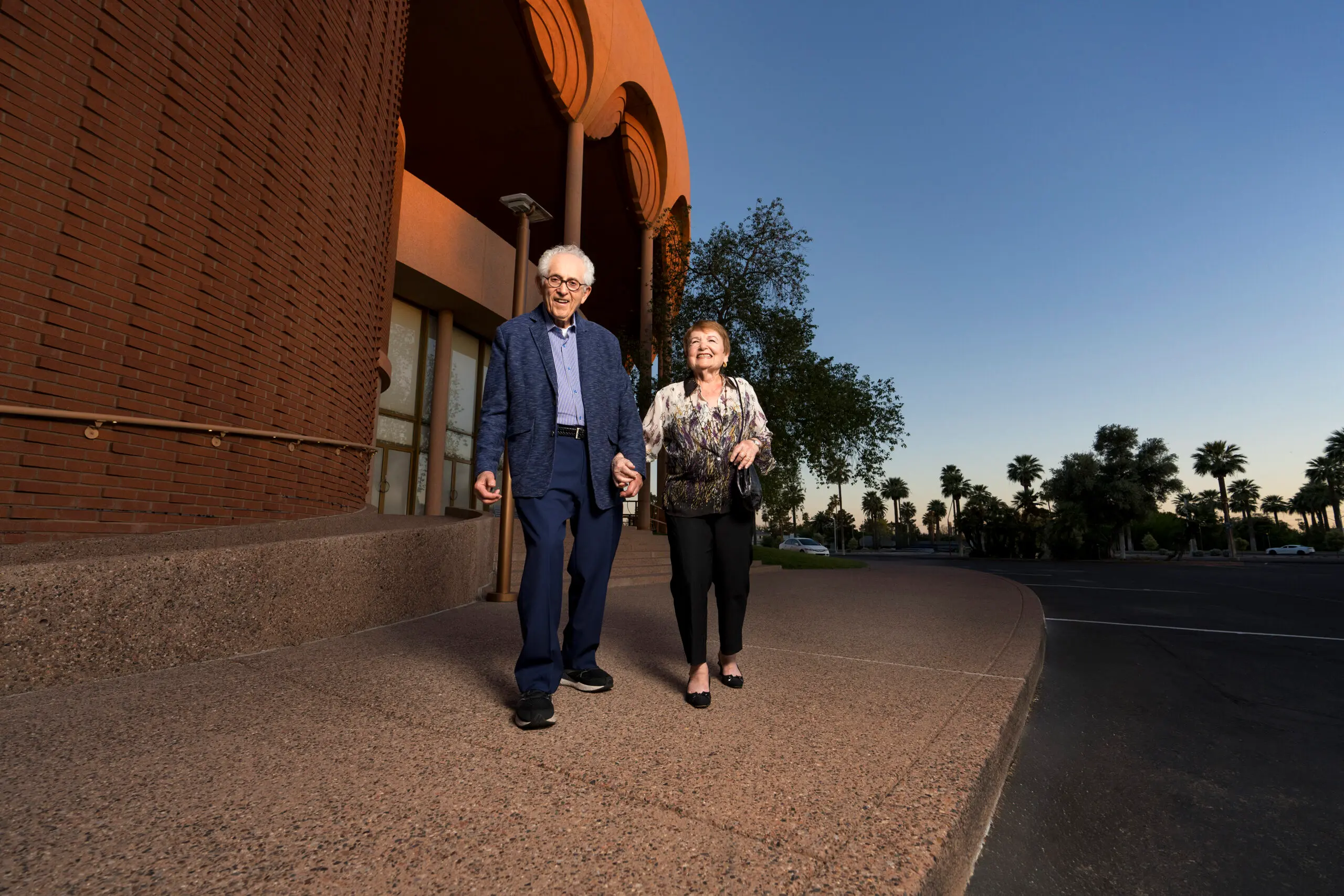 A smiling couple walks out of the theater at dusk.
